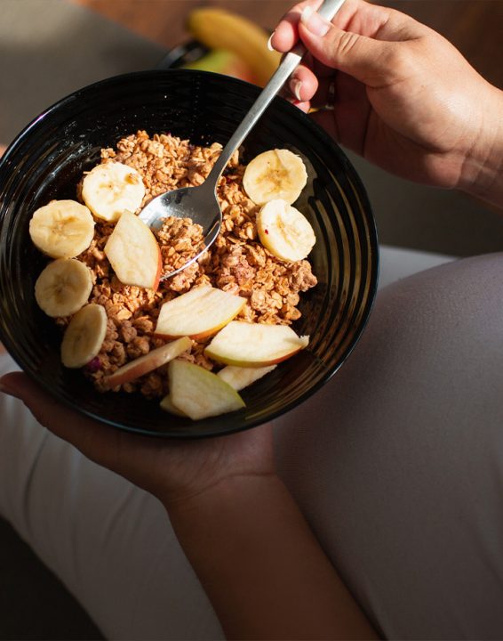 Donna in gravidanza che mangia cereali con mele e banane: una corretta dieta ricca di fibre